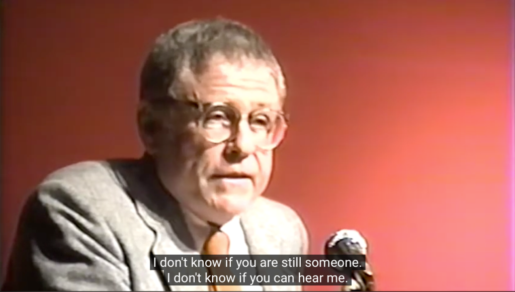 Screen shot of Robert Mezey at the microphone. The caption reads: I don't know if you are still someone. I don't know if you can hear me.
